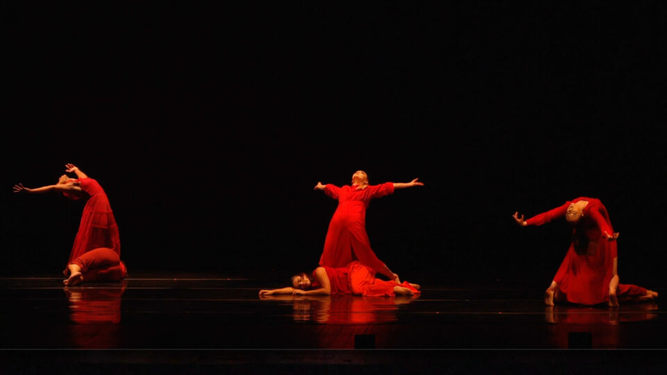 Six dancers on stage in red gowns