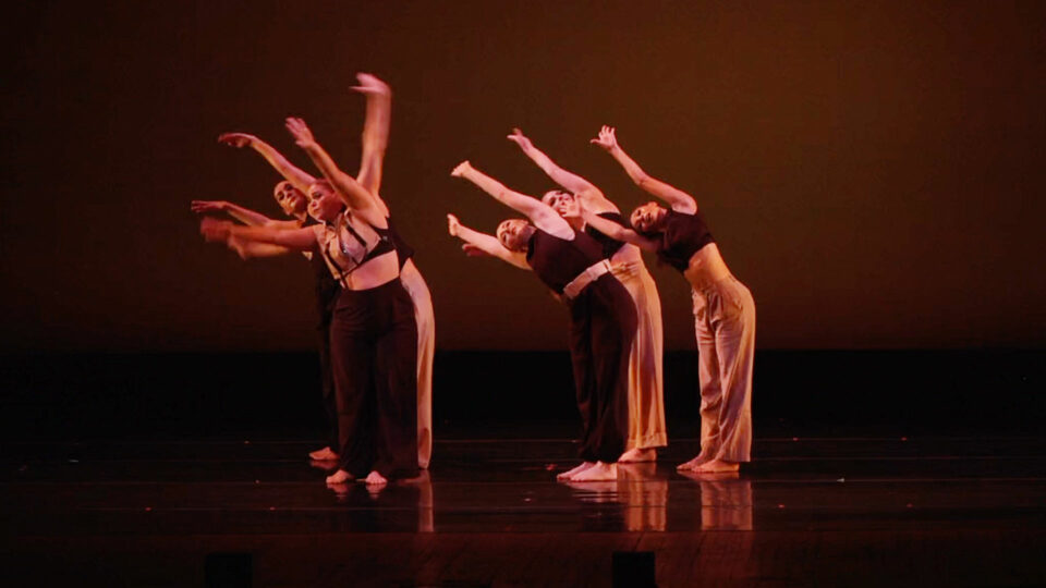 Six dancers on stage with arms extend